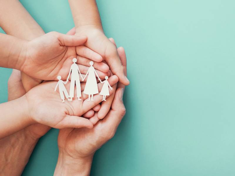 three sets of hands cupping a cutout of a family